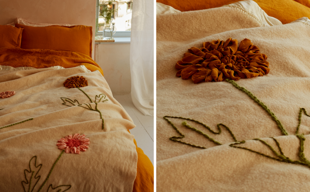 A pale coverlet on a bed with bright, textured embroidered flowers